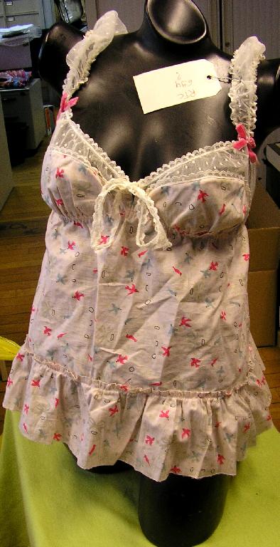 BLOUSE POUR FEMMES CONFECTIONNÉE EN TISSU LÉGER 100% COTON IMPRIMÉ, DESCENDANT JUSQU'AUX HANCHES, ÉVASÉE VERS LA BASE. 

CETTE BLOUSE COMPORTE DES BRETELLES ÉLASTIQUÉES SUR LEUR POURTOUR ORNÉES D'UN NŒUD DÉCORATIF, UNE ENCOLURE EN V TRÈS DÉCOLLETÉE, UNE PETITE OUVERTURE PARTIELLE AU MILIEU DU DÉCOLLETÉ SE FERMANT PAR DEUX RUBANS DE DENTELLE À NOUER, DES DÉCOUPES-POITRINE, UN ÉLÉMENT RESSERRANT SOUS LA POITRINE ET UN VOLANT D'ENVIRON 11 CM RAPPORTÉ AU BAS DE LA BLOUSE. LES BRETELLES AINSI QUE LE BORD SUPÉRIEUR DE L'ENCOLURE ET DU DOS SONT CONFECTIONNÉS EN DENTELLE. 

LA BASE DE LA BLOUSE EST SURFILÉE.