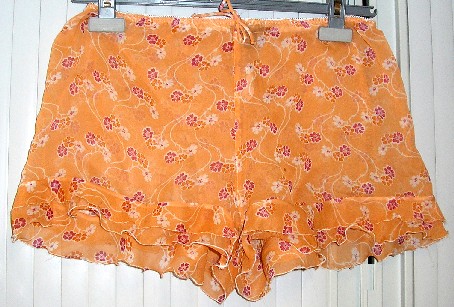 SHORT POUR FEMMES EN TISSU 100% SOIE, TRANSLUCIDE GENRE VOILE, IMPRIMÉ DE FLEURS, PRÉSENTANT UN BORD ÉLASTIQUE À LA TAILLE, UN NŒUD DÉCORATIF AU MILIEU DE LA TAILLE ET UN DOUBLE VOLANT RAPPORTÉ SUR LE POURTOUR DE LA BASE (LARGEUR : ENVIRON 5 CM).
