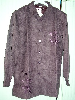 VESTE POUR FEMMES, CONFECTIONNÉE EN TISSU DE FIBRES SYNTHÉTIQUES (POLYESTER), TEINT UNIFORMÉMENT, D'ASPECT SUÉDÉ, CONSTITUÉE DE DEUX PANNEAUX FRONTAUX ET DE DEUX PANNEAUX DORSAUX COUSUS ENSEMBLE DANS LE SENS DE LA LONGUEUR, DE FORME DROITE, NON DOUBLÉE ET DESCENDANT SOUS LES HANCHES.

ELLE COMPORTE UN COL CHEMISE, UNE OUVERTURE COMPLÈTE SUR LE DEVANT SE FERMANT CÔTÉ DROIT SUR GAUCHE PAR DES BOUTONS, DES MANCHES LONGUES POURVUES D'UN POIGNET BOUTONNÉ À LEUR EXTRÉMITÉ, DES ÉPAULETTES, DEUX POCHES PLAQUÉES SUR LE DEVANT SITUÉES AU-DESSOUS DE LA TAILLE ET UN OURLET À LA BASE.

EN OUTRE, CETTE VESTE PRÉSENTE UN MOTIF BRODÉ FIGURANT DES FLEURS SUR LA POITRINE CÔTÉ GAUCHE ET DEUX FENTES LATÉRALES À LA BASE (SUR ENVIRON 11 CM).