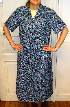 ROBE EN TISSU 100 % COTON, IMPRIMÉ DE MOTIFS FLEURIS, DESCENDANT JUSQU'À MI-MOLLET, COMPORTANT UN COL TAILLEUR, DES MANCHES COURTES, UNE OUVERTURE COMPLÈTE SUR LE DEVANT SE FERMANT DROITE SUR GAUCHE PAR DES BOUTONS, UN RUBAN CONFECTIONNÉ DANS LE MÊME TISSU À NOUER AUTOUR DE LA TAILLE, DEUX POCHES PLAQUÉES SUR LE DEVANT AU-DESSOUS DE LA TAILLE, DEUX PLIS SUR LE DEVANT PARTANT DE LA BASE DES POCHES ET DESCENDANT JUSQU'À LA BASE ET UN OURLET À LA BASE DU VÊTEMENT.