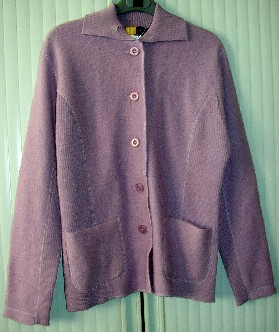 VESTE POUR FEMMES, CONFECTIONNÉE EN ÉTOFFE DE BONNETERIE DE LAINE (GENRE LAINE BOUILLIE), TEINTE UNIFORMÉMENT, CONSTITUÉE DE QUATRE PANNEAUX FRONTAUX ET DE TROIS PANNEAUX DORSAUX COUSUS ENSEMBLE DANS LE SENS DE LA LONGUEUR ET DESCENDANT SUR LES HANCHES.
ELLE PRÉSENTE UN COL, UNE OUVERTURE COMPLÈTE SUR LE DEVANT SE FERMANT CÔTÉ DROIT SUR GAUCHE PAR DES BOUTONS, DES MANCHES LONGUES OURLÉES À LEUR EXTRÉMITÉ ET DEUX POCHES PLAQUÉES SUR LE DEVANT AU-DESSOUS DE LA TAILLE.

EN OUTRE, CETTE VESTE PRÉSENTE PLUSIEURS PARTIES CONFECTIONNÉES EN MAILLES CÔTELÉES À SAVOIR : LE COL, LE DESSOUS DES MANCHES ET LES PANNEAUX LATÉRAUX.

LA BASE DU VÊTEMENT EST SURFILÉE.