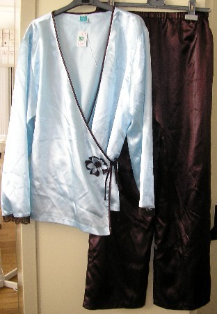 PYJAMA POUR FEMMES CONFECTIONNÉ EN TISSU DE FIBRES SYNTHÉTIQUES, D'ASPECT SATINÉ, COMPOSÉ DE DEUX VÊTEMENTS ASSORTIS, DE COUPE AMPLE ET SANS ÉLÉMENTS D'INCONFORT, COMPRENANT : 

- UN PANTALON TEINT UNIFORMÉMENT, DESCENDANT JUSQU'AUX CHEVILLES, DE COUPE AMPLE ET DROITE, SANS OUVERTURE, AVEC UN BORD ÉLASTIQUE À LA TAILLE ET UN OURLET À L'EXTRÉMITÉ DES JAMBES.

- UN VÊTEMENT DESTINÉ À RECOUVRIR LA PARTIE SUPÉRIEURE DU CORPS, GENRE VESTE, TEINT UNIFORMÉMENT MAIS D'UNE AUTRE COULEUR QUE LE PANTALON, DESCENDANT SUR LES HANCHES. 
CETTE VESTE COMPORTE DES MANCHES LONGUES BORDÉES D'UN GALON DE DENTELLE DE COULEUR CONTRASTÉE À LEUR EXTRÉMITÉ, UNE OUVERTURE COMPLÈTE SUR LE DEVANT, UN BIAIS EN SATIN DE COULEUR CONTRASTÉE BORDANT LE POURTOUR DE L'ENCOLURE ET DE L'OUVERTURE QUI SE PROLONGE PAR DEUX LIENS À NOUER PERMETTANT DE FERMER LA VESTE DROITE SUR GAUCHE, FAÇON CACHE-CŒUR, ET UNE FLEUR DÉCORATIVE BICOLORE SUR LE DEVANT AU NIVEAU DE LA TAILLE.
LE BIAIS BORDANT L'ENCOLURE ET L'OUVERTURE DE LA VESTE AINSI QUE LES LIENS À NOUER SONT DE LA MÊME COULEUR QUE LE PANTALON. 
LA BASE DE LA VESTE EST OURLÉE.