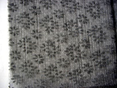 TISSU EN CREPE DE SOIE (100 %), TEINT, COMPORTANT UN FLOCAGE DE FIBRES DE VISCOSE OU DE POLYAMIDE FORMANT DES DESSINS (FLEURS). CE TISSU EST PRESENTE EN ROULEAU D’UNE LARGEUR DE 135 CM.