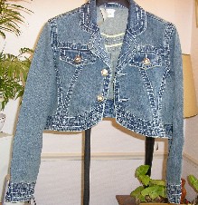 VETEMENT POUR FEMME, GENRE PETITE VESTE, EN TISSU DE COTON DIT DENIM (98% COTON – 2% ELASTHANE), DESTINE A COUVRIR LA PARTIE SUPERIEURE DU CORPS, DESCENDANT SUR LES COTES JUSTE A LA TAILLE, AVEC UN COL TAILLEUR DONT LES REBORDS SONT ARRONDIS, AVEC DES MANCHES LONGUES POURVUES A LEURS EXTREMITES D’UN POIGNET DE FORME ARRONDIE SE FERMANT A L’AIDE DE DEUX BOUTONS EN METAL, AVEC UNE OUVERTURE COMPLETE SUR LE DEVANT SE FERMANT GAUCHE SUR DROITE A L’AIDE DE BOUTONS EN METAL, AVEC UNE POCHE DE CHAQUE COTE AU NIVEAU DE LA POITRINE DOTEE DE RABAT SE FERMANT A L’AIDE DE BOUTONS EN METAL, SANS DOUBLURE, AVEC UNE BASE ARRONDIE DANS LE DOS REMONTANT EN SON MILIEU EN POINTE ET SUR LE DEVANT REMONTANT DES COTES JUSQU’AU NIVEAU DE LA POITRINE, AVEC UN OURLET A LA BASE.

LE COL, LES POIGNETS DES MANCHES ET LA BASE DE LA VESTE SONT DOTES DE LARGES SURPIQURES.
LE DOS COMPORTE QUATRE PANNEAUX DORSAUX ET LE DEVANT DEUX PANNEAUX FRONTAUX DE CHAQUE COTE.