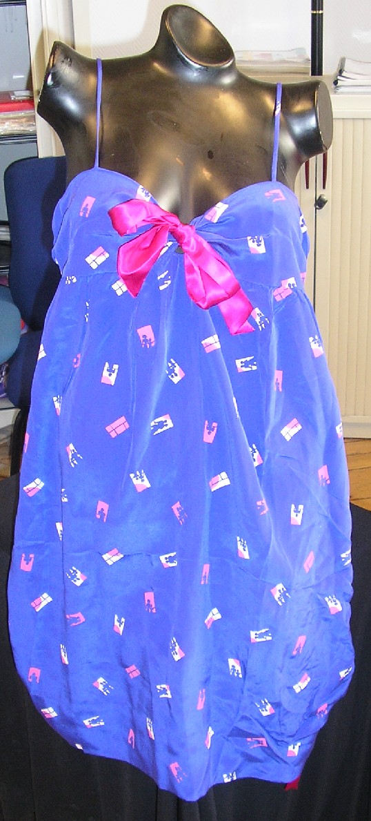 ROBE POUR FEMMES EN TISSU SATINÉ DE SOIE, IMPRIMÉ, DESCENDANT JUSQU'AUX GENOUX, SANS MANCHES, AVEC UNE ENCOLURE EN V DÉCOLLETÉE, AVEC UN NOEUD DE COULEUR CONTRASTÉE AU MILIEU DU DÉCOLLETÉ, AVEC DE FINES BRETELLES, AVEC UN AUTRE NOEUD EN BAS À GAUCHE, AVEC UN OURLET À LA BASE.