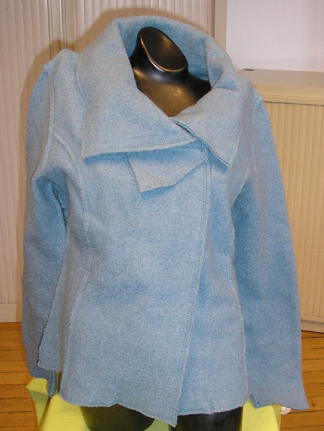VESTE POUR FEMMES, CONFECTIONNÉE EN ÉTOFFE DE BONNETERIE DE LAINE BOUILLIE, CONSTITUÉE DE QUATRE PANNEAUX FRONTAUX ET DE TROIS PANNEAUX DORSAUX COUSUS ENSEMBLE DANS LE SENS DE LA LONGUEUR ET DESCENDANT JUSQU'AUX HANCHES. 

ELLE COMPORTE UN COL CHEMISIER, UNE OUVERTURE COMPLÈTE SUR LE DEVANT SE FERMANT CÔTÉ DROIT SUR CÔTÉ GAUCHE AU MOYEN DE DEUX BOUTONS PRESSION DISPOSÉS HORIZONTALEMENT, DES MANCHES LONGUES AINSI QU'UN OURLET À LA BASE ET À L'EXTRÉMITÉ DES MANCHES.