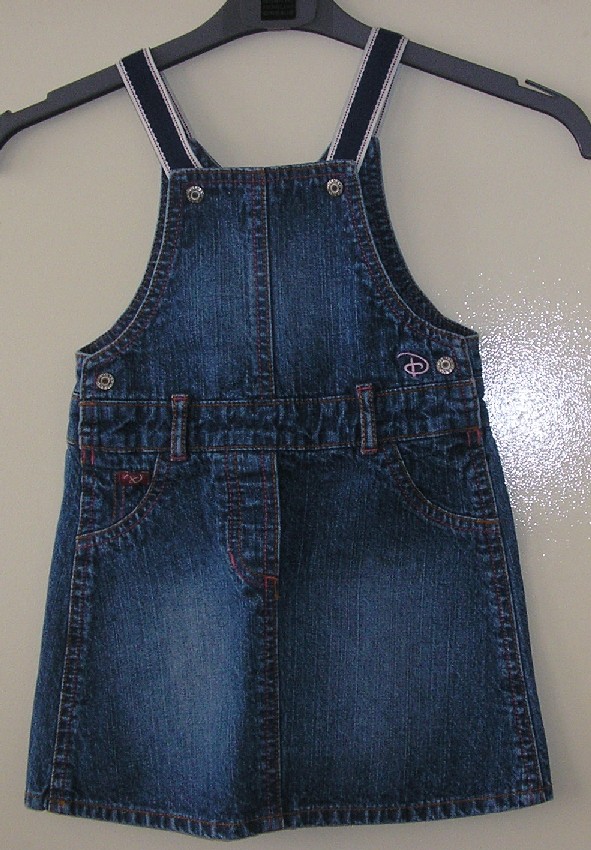 VÊTEMENT POUR FILLETTES, TYPE JUPE-BAVETTE , EN TISSU DE COTON DIT DENIM (100% COTON).
CETTE JUPE COMPORTE UNE BAVETTE DANS LE DOS ET UNE AUTRE SUR LE DEVANT RELIÉES AU MOYEN DE BRETELLES CONFECTIONNÉES DANS UN AUTRE TISSU ET S’ATTACHANT SUR LE DEVANT À L'AIDE D'UN BOUTON- PRESSION EN MÉTAL. 
ELLE COMPORTE AUSSI DEUX PETITES OUVERTURES SUR LES CÔTÉS SE FERMENT AU MOYEN D'UN BOUTON-PRESSION EN MÉTAL, UN PASSE CEINTURE, UNE BRODERIE SUR LE DEVANT, DEUX ÉTIQUETTES COUSUES, UNE DEVANT ET UNE DERRIÈRE ET UN OURLET À LA BASE.