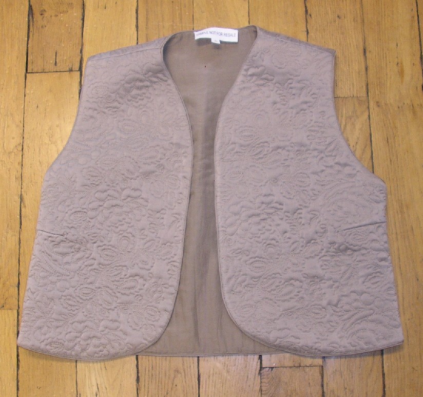 GILET UNICOLORE EN TISSU MATELASSÉ DE SOIE, LES COUTURES FORMANT UN MOTIF FLORAL, DESTINÉ À RECOUVRIR LA PARTIE SUPÉRIEURE DU CORPS, DESCENDANT JUSQU'AUX HANCHES, AVEC UNE ENCOLURE EN V SANS COL, SANS MANCHES, AVEC UNE OUVERTURE COMPLÈTE SUR LE DEVANT, AVEC UNE DOUBLURE COMPLÈTE, AVEC UN GALON TON SUR TON SUR TOUT LE PORTOUR.