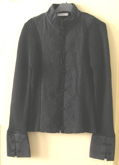VESTE POUR FEMMES, CONSTITUÉE DE TROIS PANNEAUX COUSUS ENSEMBLE DANS LE SENS DE LA LONGUEUR (2 PANNEAUX FRONTAUX ET UN PANNEAU DORSAL), CONFECTIONNÉE MAJORITAIREMENT EN ÉTOFFE DE BONNETERIE DE COTON, À MAILLES CÔTELÉES ET TEINTE UNIFORMÉMENT, ET DESCENDANT JUSQU'AUX HANCHES.

CETTE VESTE PRÉSENTE UN COL MONTANT EN TISSU, UNE OUVERTURE COMPLÈTE SUR LE DEVANT SE FERMANT DROITE SUR GAUCHE PAR DES AGRAFES, UN EMPIÈCEMENT DE TISSU DE PART ET D'AUTRE DE L'OUVERTURE ET DES MANCHES LONGUES MUNIES À LEUR EXTRÉMITÉ D'UN POIGNET EN TISSU FENDU SE FERMANT PAR DEUX AGRAFES.

LE TISSU UTILISÉ POUR LE COL, L'OUVERTURE ET LES POIGNETS EST À ARMURE SERGÉ (ASPECT DENIM) ET PRÉSENTE DES BRODERIES DÉCORATIVES.