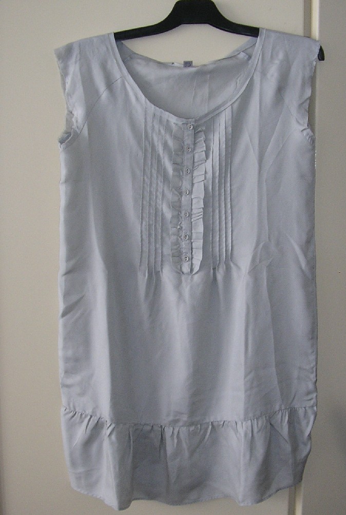 VÊTEMENT POUR FEMMES, TYPE BLOUSE, CONFECTIONNÉ EN TISSU DE SOIE, LÉGER, DE FORME AMPLE, UNICOLORE, DESTINÉ À RECOUVRIR LA PARTIE SUPÉRIEURE DU CORPS, DESCENDANT JUSQU'AU DESSOUS DES HANCHES, AVEC UNE ENCOLURE RONDE, AVEC UNE OUVERTURE PARTIELLE SUR LE DEVANT FERMANT DROITE SUR GAUCHE AU MOYEN DE BOUTONS, SANS MANCHES, AVEC UN OURLET À LA BASE.