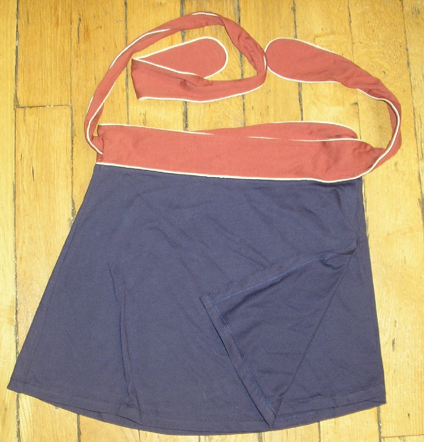 JUPE POUR FEMMES, CONFECTIONNÉE EN ÉTOFFE DE BONNETERIE DE COTON, DESCENDANT JUSQU'À LA MI-CUISSE, DE TYPE JUPE PORTE FEUILLE. 
ELLE SE PRÉSENTE SOUS LA FORME D'UN RECTANGLE D'ÉTOFFE AU SOMMET DUQUEL UN EMPIÈCEMENT DE FORME PLUS LONGUE ET DE COULEUR CONTRASTÉE A ÉTÉ COUSU, FORMANT AINSI DEUX LIENS AUX EXTRÉMITÉS.
CETTE PIÈCE D'ÉTOFFE EST ENROULÉE AUTOUR DE LA TAILLE ET FIXÉE EN NOUANT LES DEUX CORDONS.
