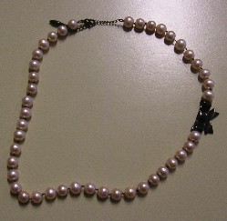 COLLIER DE PERLES DE CULTURE AVEC UN FERMOIR AINSI QU'UNE DECORATION EN FORME DE NŒUD EN METAL COMMUN.
