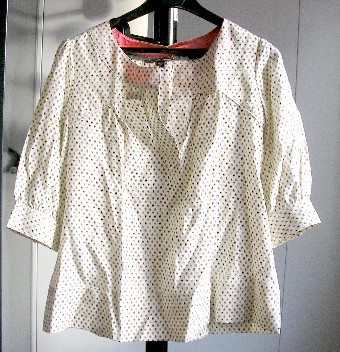 VETEMENT POUR FEMME, GENRE BLOUSE, DE FACTURE AMPLE, EN TISSU DE SOIE (60% SOIE – 40% COTON), DESTINE A COUVRIR LA PARTIE SUPERIEURE DU CORPS, DESCENDANT JUSQU’AUX HANCHES, AVEC UNE ENCOLURE ARRONDIE, AVEC UNE OUVERTURE PARTIELLE SUR LE DEVANT SANS SYSTEME DE FERMETURE, AVEC DES MANCHES 3/4 DOTEES A LEURS EXTREMITES D’UN POIGNET SE FERMANT A L’AIDE DE GANSES ET DE BOUTONS, AVEC UNE LARGE BANDE RAJOUTEE A LA BASE FORMANT OURLET.