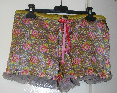 PETIT SHORT D’INTERIEUR POUR FEMME, DE FACTURE AMPLE ET FLUIDE, TRES ELABORE, EN TISSU DE SOIE (100% SOIE), AVEC UN ELASTIQUE A LA TAILLE UNIQUEMENT DANS LE DOS, AVEC UNE BANDE RAJOUTEE A LA TAILLE SUR LE DEVANT DOTEE D’UN CORDON COULISSANT RESSERRANT FORMANT LIEN A NOUER EN VELOURS, SANS OUVERTURE SUR LE DEVANT, AVEC UN VOLANT EN MOUSSELINE A LA BASE DES JAMBES, SANS FOND INTERNE A L’ENTREJAMBE.