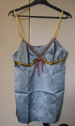 VETEMENT POUR FEMME, GENRE BLOUSE-CARACO, DE FACTURE AMPLE ET FLUIDE, TRES ELABOREE, EN TISSU DE SOIE (100% SOIE) DESTINE A COUVRIR LA PARTIE SUPERIEURE DU CORPS, DESCENDANT JUSQU’AUX HANCHES, AVEC DEUX FINES BRETELLES REGLABLES, AVEC UN EMPIECEMENT DOTEE D’UNE ENCOLURE EN « V » GARNIE D’UN VOLANT EN MOUSSELINE, AVEC UN RUBAN DE SATIN ET UN NOEUD EN VELOURS SOUS LA POITRINE, AVEC UNE LARGE BANDE RAJOUTEE A LA BASE FORMANT OURLET.

LONGUEUR : 66 CM