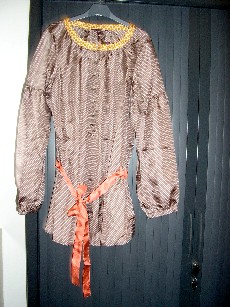 VETEMENT DESTINE A RECOUVRIR LA PARTIE SUPERIEURE DU CORPS, GENRE TUNIQUE, POUR FEMMES, D'UNE LONGUEUR DE 80 CM POUR LA TAILLE 40, EN TISSU 100% SOIE, COMPORTANT UNE ENCOLURE ARRONDIE, UNE OUVERTURE PARTIELLE SUR LE DEVANT AU MILIEU AVEC DES BOUTONS SE FERMANT DE DROITE SUR GAUCHE, DES MANCHES LONGUES DONT LES EXTREMITES SE TERMINENT PAR UN BIAIS AVEC UNE OUVERTURE ET UN BOUTON, DES PASSANTS POUR CEINTURE ET UNE CEINTURE A NOUER AU NIVEAU DE LA TAILLE, LA BASE DU VETEMENT EST OURLEE.