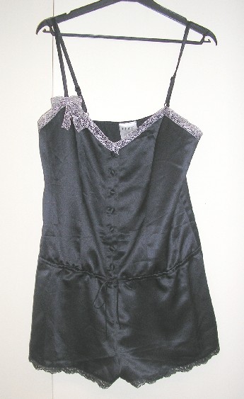 VÊTEMENTS POUR FEMMES SE PRESENTANT SOUS LA FORME D'UN CARACO ET UNE CULOTTE, CONFECTIONNE D’UNE SEULE PIECE, EN TISSU D'ASPECT SATINÉ DE FIBRES SYNTHÉTIQUES (100% POLYESTER), TEINT UNIFORMÉMENT, DESTINE A COUVRIR LA PARTIE SUPERIEURE ET INFERIEURE DU CORPS, IL DESCEND JUSQU'A MI-CUISSES. 

CE VETEMENT PRESENTE SUR LE HAUT UN GENRE CARACO, AVEC UNE ENCOLURE EN « V » DÉCOLLETÉE, DOTEE D’UN GALON EN DENTELLE SE PROLONGEANT PAR UN NŒUD DECORATIF SUR LE DEVANT, AVEC DE FINES BRETELLES RÉGLABLES, AVEC UNE OUVERTURE PARTIELLE SUR LE DEVANT SE FERMANT DROITE SUR GAUCHE A L’AIDE BOUTONS.

IL PRESENTE EGALEMENT SUR LE BAS UN GENRE SHORT, AVEC UN LIEN A NOUER A LA TAILLE RELIANT LE HAUT ET LE BAS, SANS OUVERTURE AUX ENTRE-JAMBES, AVEC UN GALON EN DENTELLE SUR LE POURTOUR A LA BASE.