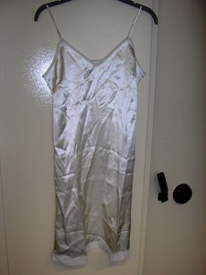 COMBINAISON POUR FEMMES, GENRE FOND DE ROBE, EN TISSU DE SOIE, UNI, LÉGÈREMENT ÉVASÉE, DESCENDANT A MI-CUISSES ET COMPORTANT DE FINES BRETELLES RÉGLABLES, UN PROFOND DÉCOLLETÉ EN V BORDÉ PAR UN GALON DE VOILE SE PROLONGEANT SUR LE POURTOUR DES EMMANCHURES ET DU DOS ET DES PINCES POITRINE.  LA BASE DE LA COMBINAISON COMPORTE UNE BANDE EN VOILE.