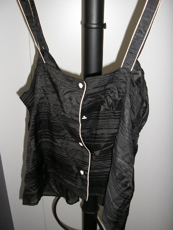 VETEMENT POUR FEMMES, GENRE BLOUSE-CARACO, DE FACTURE FLUIDE, EN TISSU DE SOIE MAJORITAIRE (67% SOIE ET 33% COTON), LEGEREMENT TRANSPARENT ET DE COULEUR NOIRE, DESTINE A COUVRIR LA PARTIE SUPERIEURE DU CORPS ET DESCENDANT JUSQU’AUX HANCHES. IL COMPORTE DEUX BRETELLES SE FERMANT A L'AIDE D'UN BOUTON BLANC, UNE OUVERTURE COMPLETE DANS LE DOS SE FERMANT DROITE SUR GAUCHE AU MOYEN DE QUATRE BOUTONS BLANCS. LE VETEMENT EST DOTE D'UNE ENCOLURE EN « V » ET D'UN ELASTIQUE SOULIGNANT LA POITRINE; LA BASE DU VETEMENT EST OURLEE.