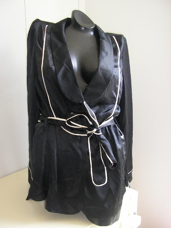 VÊTEMENT POUR FEMMES, GENRE VESTE D'INTÉRIEUR, CONFECTIONNÉ EN TISSU DE SOIE (100%), DESTINÉ A RECOUVRIR LA PARTIE SUPÉRIEURE DU CORPS, DE CONTEXTURE LÉGÈRE, AVEC UN LARGE COL CHEMISIER ARRONDI ET DES MANCHES LONGUES. LA VESTE COMPORTE UNE OUVERTURE COMPLÈTE SUR LE DEVANT ET SE FERME DROITE SUR GAUCHE A L'AIDE DE 3 BOUTONS ET D'UNE CEINTURE A NOUER, MAINTENUE PAR 2 PASSANTS COUSUS DANS LE DOS. LA BASE DU VÊTEMENT ET LES EXTRÉMITÉS DES MANCHES SONT OURLÉES.