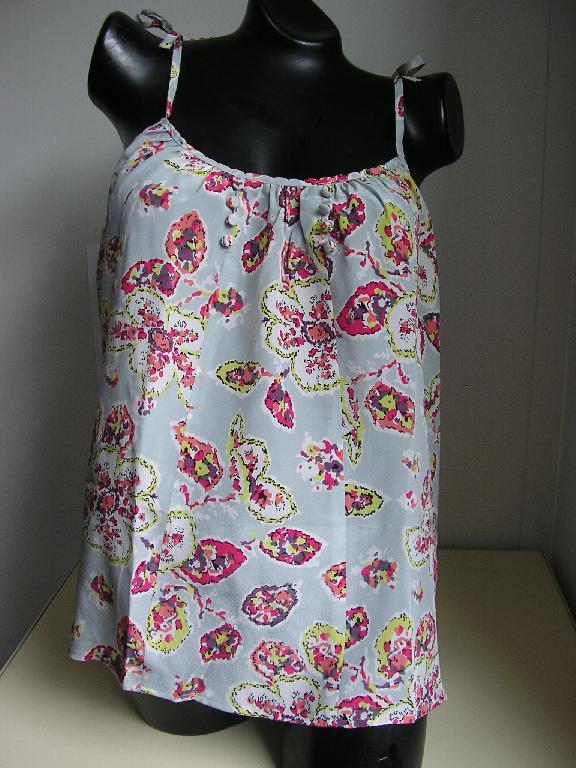 VÊTEMENT POUR FEMMES, GENRE BLOUSE, CONFECTIONNÉ EN TISSU DE SOIE(100%), DE FACTURE AMPLE ET FLUIDE, DESTINÉ À RECOUVRIR LA PARTIE SUPÉRIEURE DU CORPS, DESCENDANT JUSQU'AUX HANCHES, AVEC UNE ENCOLURE DROITE, SANS MANCHES, SANS OUVERTURE, AVEC DE FINES BRETELLES A NOUER, ET AVEC UN OURLET A LA BASE. EN OUTRE, LA BLOUSE PRÉSENTE UN BIAIS DÉCORATIF SUR TOUT LE POURTOUR DU VÊTEMENT ET DES PETITS BOUTONS SOUS L'ENCOLURE.
