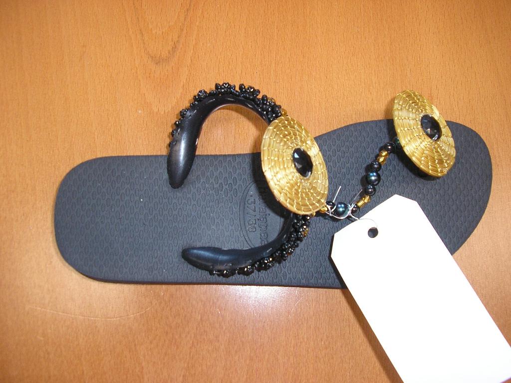 CHAUSSURE, DU STYLE TONG, AVEC UN DESSUS EN MATIÈRE PLASTIQUE. LES LANIÈRES SONT FIXÉES PAR DES TETONS EN TROIS POINTS À LA SEMELLE DONT UN POINT ENTRE LE POUCE ET LES AUTRES ORTEILS ET LES DEUX AUTRES POINTS SUR LES COTES, ILS SONT VISIBLES SUR LA SEMELLE EXTERIEURE, AVEC UNE SEMELLE EXTÉRIEURE EN CAOUTCHOUC DOTEE DE STRIES ANTIDERAPANTES. CETTE CHAUSSURE LAISSE LE TALON ET LES DOIGTS DE PIED DEGAGES.
ELLE COMPORTE DIFFÉRENTS ORNEMENTS:DES PERLES SONT COUSUES SUR LA LANIÈRE SITUÉE AU NIVEAU DU COUP DE PIED, OU ENFILÉES ENTRE LES DEUX LANIÈRES. DEUX SPIRALES EN "CAPIM DOURADO" (MATIÈRE VÉGÉTALE) SONT ÉGALEMENT COUSUES SUR LES LANIÈRES.

POINTURE 37/38