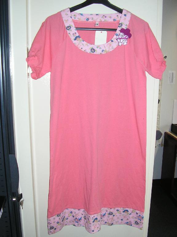 CHEMISE DE NUIT POUR FEMMES, EN ÉTOFFE DE BONNETERIE DE COTON (100%), DESCENDANT JUSQU'AUX GENOUX, DE FACTURE SOUPLE, AVEC UNE ENCOLURE ARRONDIE POURVUE D'UNE BANDE RAPPORTÉE EN BONNETERIE, AVEC DES MANCHES RAGLAN COURTES ET ÉLASTIQUÉES AUX EXTRÉMITÉS, ET AVEC UNE LARGE BANDE RAPPORTÉE DU MÊME MOTIF QUE L'ENCOLURE A LA BASE DU VÊTEMENT. EN OUTRE L'ARTICLE PRÉSENTE UNE GARNITURE, REPRÉSENTANT DEUX FLEURS DOTÉES D'UN PETIT NOEUD, COUSUE SUR LE COTÉ GAUCHE DE L'ENCOLURE.