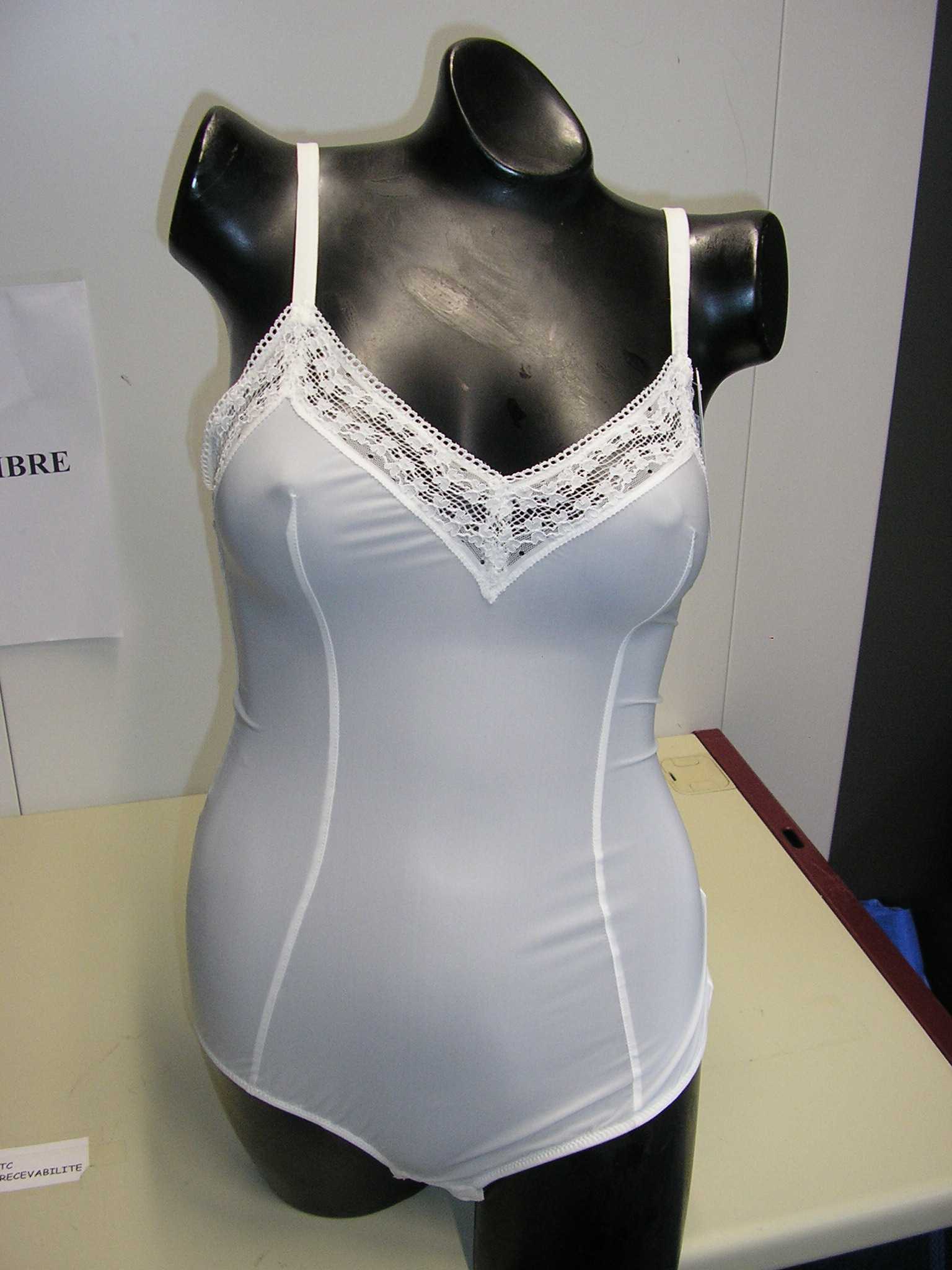 VÊTEMENT POUR FEMME, DIT "BODY", EN ÉTOFFE DE BONNETERIE DE FIBRES SYNTHÉTIQUES, PRÈS DU CORPS, DESTINÉ A COUVRIR LE HAUT DU CORPS JUSQU'A L'ENTREJAMBE. L'ARTICLE COMPORTE UNE ENCOLURE EN « V », UNE DOUBLURE A L'ENTREJAMBE, DE FINES BRETELLES RÈGLABLES, UN GALON DE DENTELLE RAPPORTÉ POURVU D'UN ÉLASTIQUE SUR LE POURTOUR DE L'ENCOLURE ET DANS LE DOS. LE VÊTEMENT PRÉSENTE ÉGALEMENT DEUX COUTURES VERTICALES SUR LE DEVANT DE LA POITRINE JUSQU'A LA BASE ET SE REFERME A L'ENTREJAMBE AU MOYEN DE TROIS PETITS BOUTONS-PRESSION.