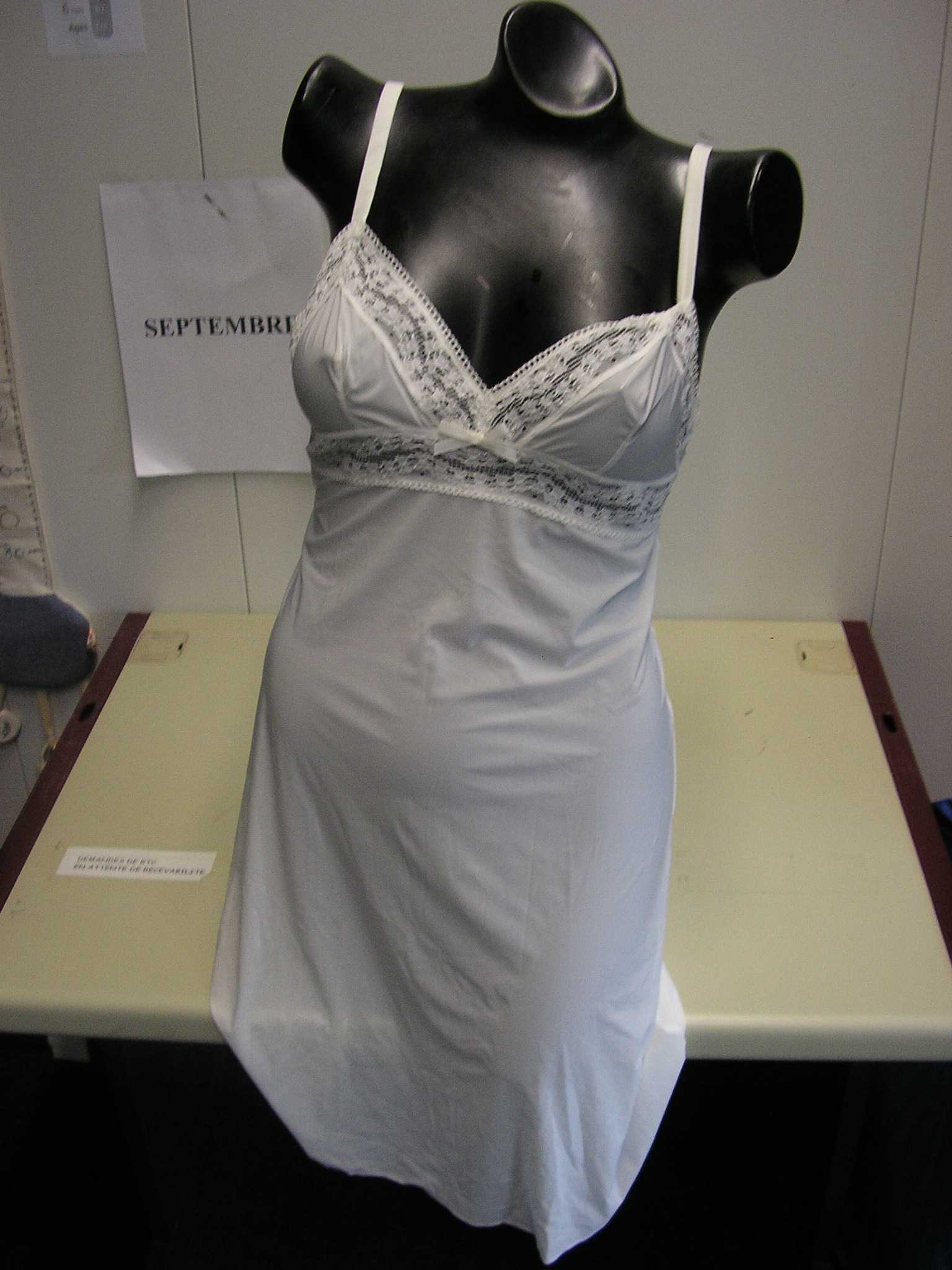 VÊTEMENT POUR FEMME, GENRE NUISETTE, CONFECTIONNÉ EN ÉTOFFE DE BONNETERIE DE FIBRES SYNTHÉTIQUES (76% POLYAMIDE, 24% ÉLASTHANNE), DESTINÉ A RECOUVRIR LE CORPS, LÉGÈREMENT CINTRÉ, AVEC UN DÉCOLLETÉ EN V, COMPORTANT DE FINES BRETELLES RÈGLABLES, UN EMPIÈCEMENT DE DENTELLE RAPPORTÉ SOUS LA POITRINE, DANS LE DOS ET SUR TOUT LE POURTOUR DE LA DÉCOUPE POITRINE. LA NUISETTE PRÉSENTE ÉGALEMENT UN NŒUD DÉCORATIF AU MILIEU DE LA POITRINE ET UN OURLET A LA BASE.