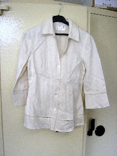 VÊTEMENT POUR FEMMES EN TISSU DE LIN (100% LIN), DESTINÉ À RECOUVRIR LA PARTIE SUPÉRIEURE DU CORPS, GENRE CHEMISIER, AJUSTÉ AU MOYEN DE PINCES, DESCENDANT JUSQU'AU DESSOUS DE LA TAILLE, AVEC UNE ENCOLURE DROITE, AVEC UN COL, AVEC DES EPAULETTES, AVEC DES MANCHES 3/4, AVEC UNE OUVERTURE COMPLÈTE SUR LE DEVANT SE FERMANT DROITE SUR GAUCHE AU MOYEN DE BOUTONS, AVEC UN CORDON A NOUER DANS LE DOS MUNI D'UNE PERLE A CHAQUE EXTREMITE, AVEC UN GALON AJOURE VERS L'EXTREMITE DES MANCHES ET DE LA BASE, AVEC UNE FENTE AUX EXTREMITES DES MANCHES, AVEC UNE BASE OURLÉE.

TAILLE 38
