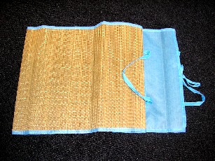 NATTE DE PLAGE, EN PAILLE, PLIABLE, COMPORTANT UN EMPIECEMENT EN TISSU, SERVANT DE RANGEMENT A LA NATTE UNE FOIS ENROULEE SUR ELLE-MEME, AVEC ANSES ET LIENS A NOUER, LES BORDURES SONT ARRETEES PAR UN BIAIS EN TISSU.