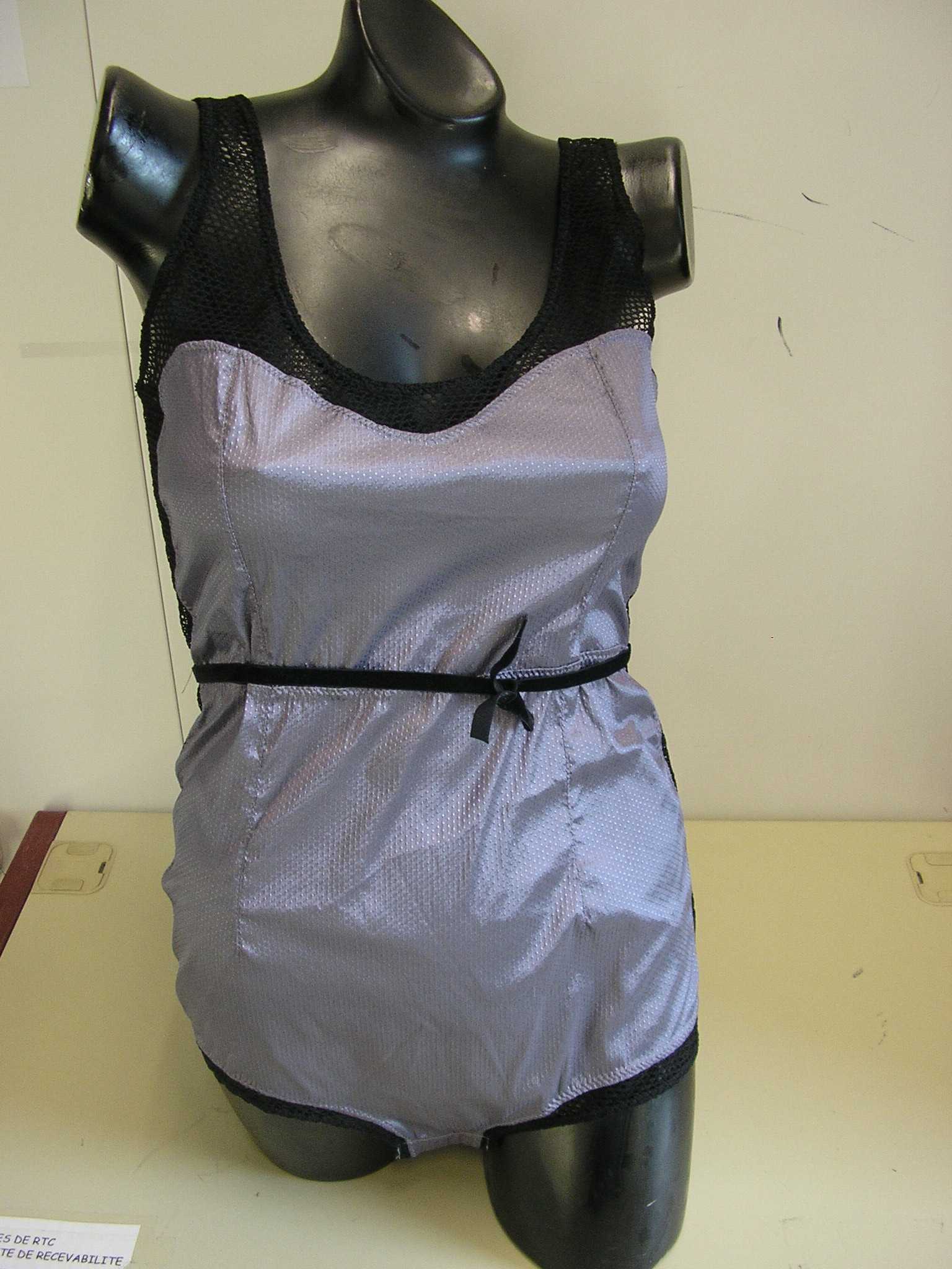 VÊTEMENT POUR FEMME, DIT "BODY", MAJORITAIREMENT EN TISSU DE FIBRES SYNTHÉTIQUES (87% POLYAMIDE, 13% ÉLASTHANNE), DESTINÉ A COUVRIR LE HAUT DU CORPS JUSQU'A L'ENTREJAMBE. LE BODY COMPORTE UNE ENCOLURE ARRONDIE, UNE DOUBLURE EN BONNETERIE A L'ENTREJAMBE, LAQUELLE SE REFERME AU MOYEN DE TROIS PETITS BOUTONS-PRESSION.
L'ENCOLURE, LES BRETELLES, LE HAUT DU DOS, LES COUTURES LATÉRALES ET LA BASE DE L'ENTREJAMBE SONT COMPOSÉS EN ÉTOFFE DE BONNETERIE ASPECT MAILLE-FILET. ENFIN, LE BODY PRÉSENTE UNE PETITE CEINTURE DE VELOURS LÉGÈREMENT ÉLASTIQUÉE, COUSUE SUR CHAQUE COTÉ ET QUI SE NOUE SUR LE DEVANT.