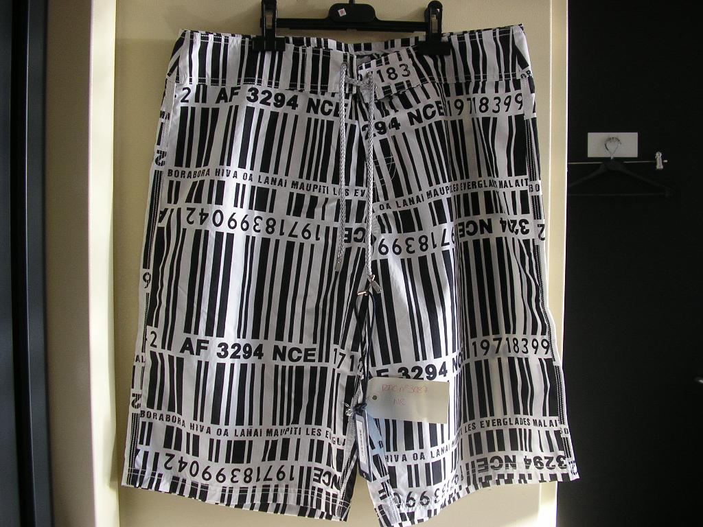 SHORT POUR HOMME, EN TISSU DE FIBRES SYNTHÉTIQUES (100% POLYAMIDE) DESCENDANT JUSQU'AUX GENOUX, AVEC UNE OUVERTURE PARTIELLE SUR LE DEVANT SE FERMANT GAUCHE SUR DROITE AU MOYEN D'UNE BANDE VELCRO DISSIMULÉE SOUS UNE PATTE DE PROTECTION ET PAR UN LACET SE NOUANT SUR LE DEVANT, AVEC UNE DOUBLURE EN BONNETERIE ASPECT MAILLE-FILET FORMANT UN SLIP, ET UN OURLET À LA BASE. LE SHORT PRÉSENTE UNE IMPRESSION FANTAISIE ET LE NOM DE LA MARQUE EST INSCRIT AU VERSO.