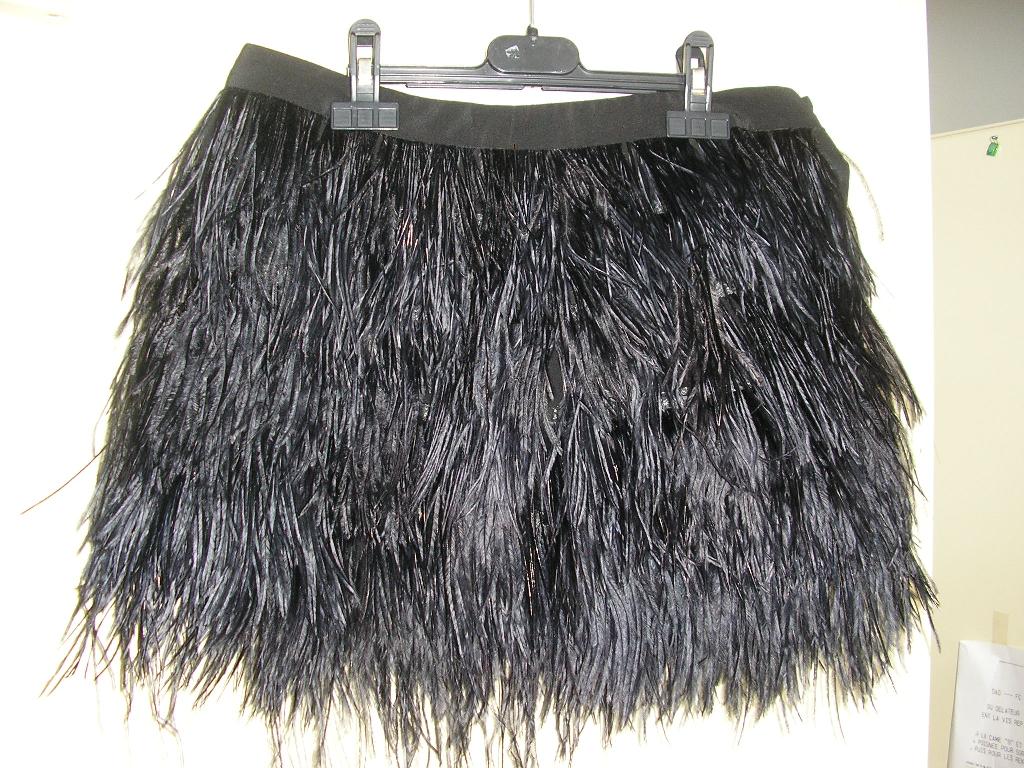 PETITE JUPE EN SOIE, ORNÉE DE PLUMES D'AUTRUCHE SUR TOUTE LA SURFACE, ET SE FERMANT SUR UN CÔTÉ AU MOYEN DE PETITES AGRAFES ET D'UN BOUTON.