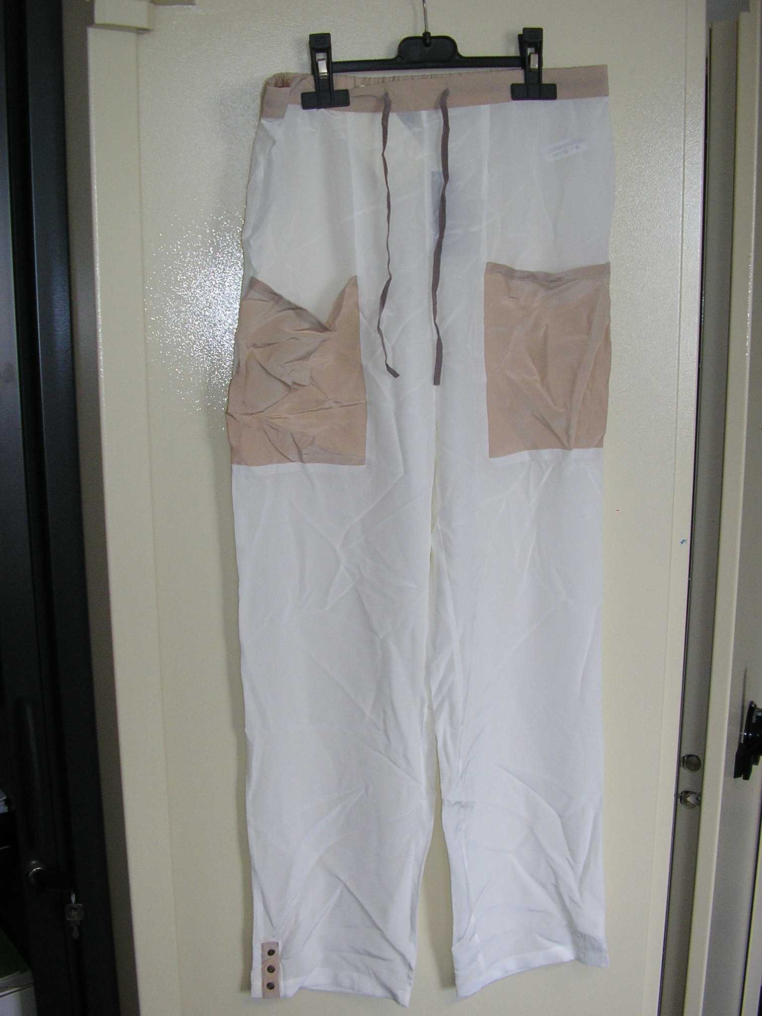 PANTALON POUR FEMMES, SANS OUVERTURE, CONFECTIONNÉ EN TISSU DE SOIE, DE FACTURE AMPLE ET FLUIDE, DESCENDANT JUSQU'AUX CHEVILLES EN ENVELOPPANT SÉPARÉMENT CHAQUE JAMBE, DONT LA TAILLE COMPORTE UN LIEN A NOUER SUR LE DEVANT ET UN DOS ÉLASTIQUÉ, ET DEUX GRANDES POCHES PLAQUÉES AU NIVEAU DES CUISSES. LA BASE DU PANTALON EST OURLÉE ET PRÉSENTE UNE PETITE FENTE SE FERMANT AU MOYEN DE TROIS PETITS BOUTONS.