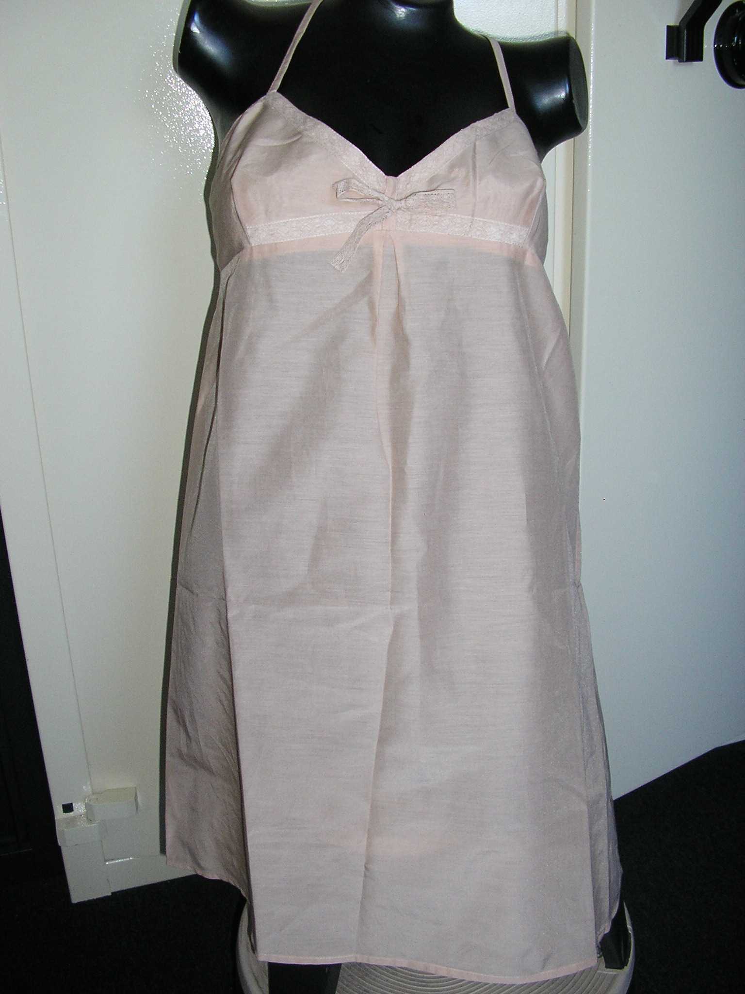 ROBE CONFECTIONNÉE EN TISSU MAJORITAIRE DE COTON (75% COTON, 25% SOIE), DE FACTURE LÉGÈRE, DESTINÉE A COUVRIR LA PARTIE SUPÉRIEURE DU CORPS, ET DESCENDANT JUSQU'À MI-CUISSES. LE VÊTEMENT COMPORTE DE FINES BRETELLES RÈGLABLES, UNE ENCOLURE EN "V" BORDÉE D'UN BIAIS ASPECT DENTELLE, UN NŒUD DÉCORATIF EN DENTELLE SOUS L'ENCOLURE ET UN OURLET A LA BASE.

LONGUEUR : 87 CM