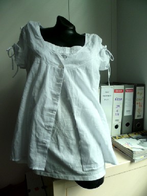 VETEMENT DESTINE A RECOUVRIR LA PARTIE SUPERIEURE DU CORPS, GENRE BLOUSE POUR FEMMES, CONFECTIONNE MAJORITAIREMENT EN TISSU VOILE DE COTON, COMPORTANT UNE ENCOLURE EN V PROFONDE BORDEE PAR UN OURLET, UNE OUVERTURE COMPLETE SUR LE DEVANT AU MILIEU AVEC DES BOUTONS SE FERMANT DE DROITE SUR GAUCHE, DES MANCHES COURTES AVEC UN LIEN RESSERRANT LA HAUTEUR À NOUER, LA BASE DU VETEMENT SE TERMINE PAR UN OURLET, AVEC A L'INTERIEUR SUR LE DEVANT UN PLASTRON EN BONNETERIE DE JERSEY COTON, SANS MANCHES, COMPORTANT UNE ENCOLURE ARRONDIE BORDEE DE DENTELLE, ET DE FINES BRETELLES.