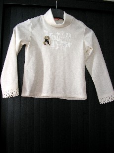 VETEMENT DESTINE A RECOUVRIR LA PARTIE SUPERIEURE DU CORPS, GENRE SOUS-PULL, POUR FILLES, EN ETOFFE DE BONNETERIE 65% POLYESTER ET 35% COTON, COMPORTANT UN COL ROULE AVEC UNE OUVERTURE SUR LE COTE GAUCHE SE PROLONGEANT SUR L'EPAULE GAUCHE AVEC DES BOUTONS-PRESSIONS, DES MANCHES LONGUES DONT LES EXTREMITES SE TERMINENT PAR UNE IMITATION DENTELLE, LA BASE DU VETEMENT EST OURLEE, AVEC MOTIFS IMPRIMES ET COUSUS AU NIVEAU DE LA POITRINE.