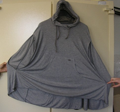 VÊTEMENT DE TYPE PONCHO DESTINE À RECOUVRIR LA PARTIE SUPÉRIEURE DU CORPS, CONFECTIONNÉ EN ÉTOFFE DE BONNETERIE LEGERE DE COTON (100% COTON), DE FACTURE AMPLE, TEINTE UNIFORMÉMENT, SANS OUVERTURE SUR LE DEVANT, AVEC UN CAPUCHON DOTE D’UNE DOUBLURE ET D’UN ELEMENT RESSERRANT SUR SON POURTOUR, AVEC UNE OUVERTURE POUR LAISSER PASSER LA TÊTE, AVEC DEUX GRANDES FENTES LATERALES PERMETTANT DE LAISSER PASSER LES BRAS, AVEC UNE POCHE VENTRALE, AVEC UN ROULOTTE DE FINITION A LA BASE.