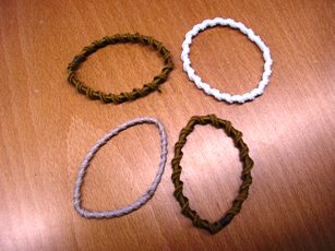 LOT DE QUINZE ANNEAUX ELASTIQUES POUR CHEVEUX CONSTITUE D'UNE SEULE LAME DE CAOUTCHOUC, DE FORME CARREE, DE 2 MM ENVIRON DE COTE, GAINEE DE BONNETERIE FORMANT UNE SPIRALE. 
LE TOUT EST PRESENTE SUR UN CARTONNAGE SOUPLE.