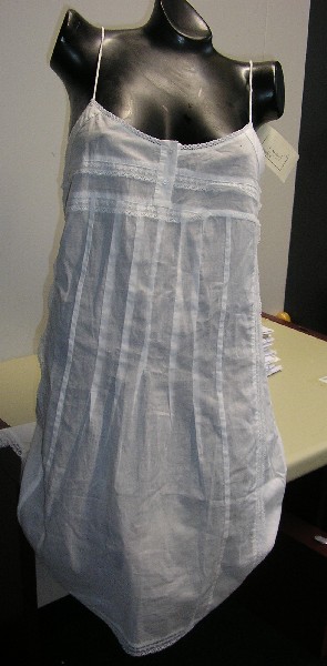 ROBE POUR FEMMES, EN TISSU DE COTON (100% COTON), DE CONTEXTURE LEGERE, DESTINEE A COUVRIR LA PARTIE SUPERIEURE DU CORPS, DESCENDANT JUSQU’AUX GENOUX, DE FORME EVASEE, AVEC UNE ENCOLURE RONDE, AVEC DEUX FINES BRETELLES REGLABLES, AVEC UN EMPIECEMENT SUR LE DEVANT, AVEC UNE OUVERTURE PARTIELLE SUR LE DEVANT SE FERMANT DROITE SUR GAUCHE A L’AIDE DE BOUTONS, AVEC UNE FENTE DE CHAQUE COTE DE 10 CM ENVIRON, AVEC UN OURLET A LA BASE DOTE D’UN GALON EN DENTELLE SUR LE POURTOUR.

CETTE ROBE PRESENTE SUR LE DEVANT ET DANS LE DOS DES NERVURES ET DES GALONS EN DENTELLE.

LONGUEUR A PARTIR DES EPAULES : 86 CM