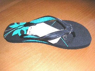 CHAUSSURE, DU STYLE TONG, NON RECONNAISSABLE COMME ÉTANT POUR HOMMES OU POUR FEMMES, AVEC UN DESSUS EN CAOUTCHOUC MUNI DE RENFORTS EN CUIR. LES LANIÈRES SONT FIXÉES PAR DES TETONS EN TROIS POINTS À LA SEMELLE DONT UN POINT ENTRE LE POUCE ET LES AUTRES ORTEILS ET LES DEUX AUTRES POINTS SUR LES COTES, AVEC UNE SEMELLE EXTÉRIEURE EN MATIERE PLASTIQUE. 
CETTE CHAUSSURE LAISSE LE TALON ET LES DOIGTS DU PIED DEGAGES, AVEC UN MOTIF DECORATIF SUR LE DESSUS DE LA SEMELLE INTERNE, AVEC UN LOGO PUBLICITAIRE SUR LES LANIERES REPRESENTANT LA MARQUE DE LA SOCIETE.