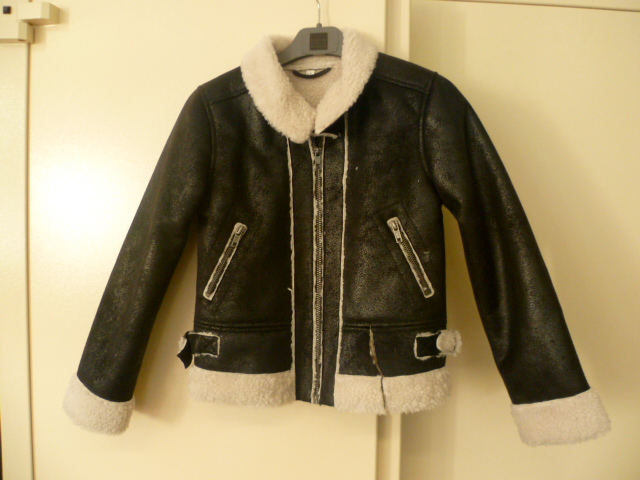 VETEMENT DESTINE A COUVRIR LA PARTIE SUPERIEURE DU CORPS, DE TYPE ARTICLE SIMILAIRE A UN BLOUSON, COMPOSE DE PLUSIEURS PANNEAUX COUSUS ENTRE EUX EN ETOFFE CONTRECOLLEE DE FIBRES SYNTHETIQUES AVEC UNE FACE EN BONNETERIE PARTIELLEMENT ENDUITE DE POLYURETHANE IMITANT LE CUIR VIEILLI ET UNE AUTRE FACE EN BONNETERIE A POILS LONGS GENRE PEAU LAINEE, AVEC DES MANCHES LONGUES RETOURNEES AUX EXTREMITES, AVEC UN COL MONTANT MUNI D'UNE PATTE DE RESSERRAGE MAINTENUE PAR DEUX ANNEAUX EN METAL, AVEC UNE POCHE LATERALE DE CHAQUE COTE AU NIVEAU DE LA TAILLE AVEC UNE FERMETURE A GLISSIERE, AVEC UNE OUVERTURE COMPLETE SUR LE DEVANT SE FERMANT BORD A BORD AU MOYEN D'UNE FERMETURE A GLISSIERE, AVEC UNE PATTE RESSERRANTE DE CHAQUE COTE DE LA BASE.  

TAILLE 8 ANS