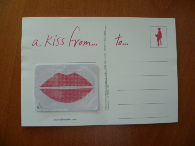 CARTE POSTALE AVEC AU RECTO LE NOM DU PRODUIT DE LA MARQUE ET LA PHOTOGRAPHIE DU MANNEQUIN ET AU VERSO UN AUTO COLLANT EN PLASTIQUE SUR LEQUEL EST DESSINE DES LEVRES IMPREGNEES DE MATIERE DE ROUGE A LEVRES AVEC UN OPERCULE DE PLASTIQUE QUI LE PROTEGE ET L' INSCRIPTION A KISS FROM...TO....
DIMENSIONS : 15,1 CM X 10,4 CM