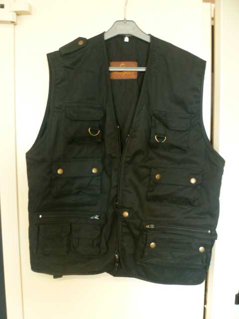 AUTRE VÊTEMENT POUR HOMME, GENRE GILET, EN TISSU (65 % POLYESTER ET 35% COTON), DE FORME AMPLE, SANS MANCHE, AVEC DE LARGES EMMANCHURES, AVEC UNE ENCOLURE EN V, AVEC UNE OUVERTURE COMPLÈTE SUR LE DEVANT SE FERMANT À L'AIDE D'UNE FERMETURE À GLISSIÈRE ET D'UNE PETITE PATTE DE BOUTONNAGE SE FERMANT GAUCHE SUR DROITE PAR BOUTON-PRESSION. LE VETEMENT COMPORTE DE MULTIPLES POCHES A SOUFFLET ET A RABBAT DE CHAQUE COTE  SUR LE DEVANT, SE FERMANT POUR LES DEUX POCHES MUNIES D'UN ANNEAU EN HAUT DU VETEMENT AVEC DES BANDES VELCRO, POUR LES DEUX POCHES INTERMEDIAIRES AVEC DES BOUTONS PRESSION ET POUR LES POCHES EN BAS DU VETEMENT AVEC DES FERMETURES À GLISSIÈRE AVEC A DROITE DEUX POCHES SUR LA POCHE SE FERMANT AVEC BANDE VELCRO ET A GAUCHE UNE POCHE SUR LA POCHE SE FERMANT PAR BOUTONS PRESSION. LE DOS DU VETEMENT EST MUNI D'UNE POCHE A SOUFFLET AVEC FERMETURE A GLISSIERE. A l'INTERIEUR DU VETEMENT  LE GILET COMPORTE DEUX POCHES LATERALES AVEC FERMETURE A GLISSIERE DE CHAQUE COTE ET DEUX POCHES A SOUFFLET A RABBAT AVEC BANDE VELCRO DE CHAQUE COTE.