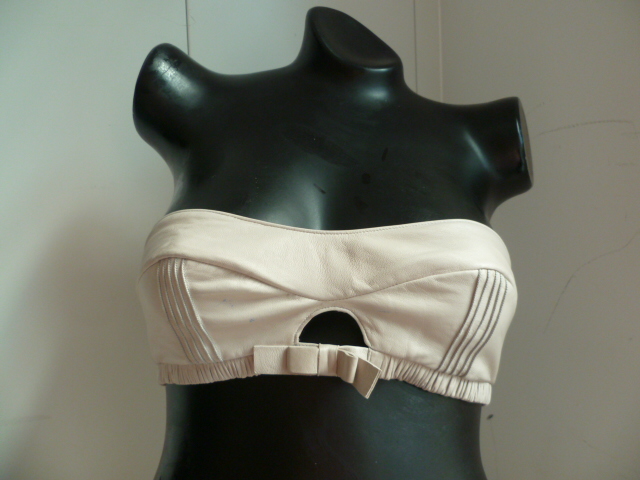 BANDEAU EN CUIR (100 % CUIR D'AGNEAU) POUR LA POITRINE, AVEC UNE DOUBLURE EN TISSU (60 % COTON – 40 % SOIE), AVEC UNE BANDE ELASTIQUEE SOUS LA POITRINE SUR LAQUELLE AU MILIEU FIGURE UN NOEUD DECORATIF ET AVEC 3 BOUTONS PRESSIONS DANS LE DOS PERMETTANT LA FERMETURE.