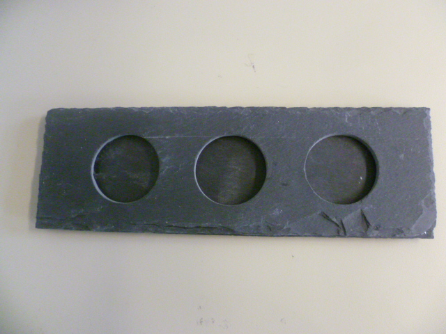 ARTICLE COMPOSE DE DEUX PLAQUES EN ARDOISE COLLEES L'UNE SUR L'AUTRE. LA PLAQUE SUPERIEURE EST PERCEE DE TROIS TROUS DE 4CM DE DIAMETRE AFIN D'Y PLACER DES BOUGIES. SOUS LA PLAQUE INFERIEURE IL Y A QUATRE TAMPONS DE PROTECTION. DIMENSION: 23X7,5 MM