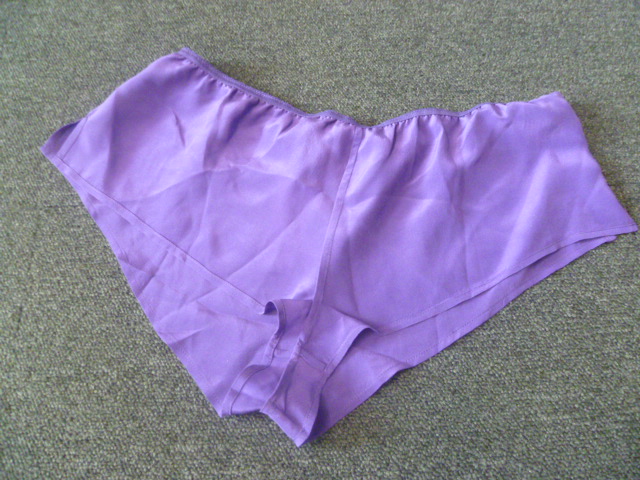 PETIT SHORT D'INTÉRIEUR POUR FEMMES, GENRE BOXER, SANS DOUBLURE ET SANS OUVERTURE, CONFECTIONNÉ EN TISSU DE SOIE, DE FACTURE AMPLE ET LÉGÈREMENT TRANSPARENT. LE VÊTEMENT COMPORTE DEUX ECHANCRURES DE 5CM SUR LES COTES, UN ÉLASTIQUE A LA TAILLE, UN PETIT CORDON  EN FORME DE NOEUD SUR LA HANCHE DROITE ET UN OURLET À LA BASE DES JAMBES.
