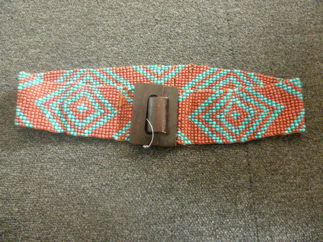 CEINTURE 100% POLYESTER COMPOSEE DE 17 RANGEES DE PERLES BICOLORES MONTEES SUR ELASTIQUE FORMANT DES MOTIFS GEOMETRIQUES. UN SYSTEME DE CROCHET EN BOIS FAIT OFFICE DE FERMETURE.