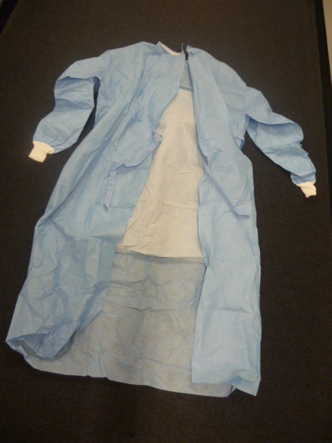 BLOUSE CHIRURGICALE (CASAQUE),RECOUVRANT LA PARTIE SUPERIEURE DU CORPS ET  DESCENDANT JUSQU'AU DESSOUS DES MOLLETS, CONFECTIONNEE PRINCIPALEMENT EN FIBRES SMS NON TISSE. LE RENFORT FRONTAL AINSI QUE CELUI DES AVANT-BRAS EST EN POLYPROPYLENE ET POLYETHYLENE. CE VETEMENT COMPORTE UNE ENCOLURE RAS-DE-COU SE FERMANT PAR UNE BANDE VELCRO AU NIVEAU DU COU, DES MANCHES LONGUES RENFORCEES PRESENTANT UN BORD-COTE EN MATIERE TEXTILE A LEUR EXTREMITE ET UNE OUVERTURE COMPLETE SUR L'ARRIERE SE FERMANT PAR DEUX LIENS AU NIVEAU DE LA TAILLE. CET ARTICLE EST ACCOMPAGNE DE DEUX ESSUIE-MAINS.